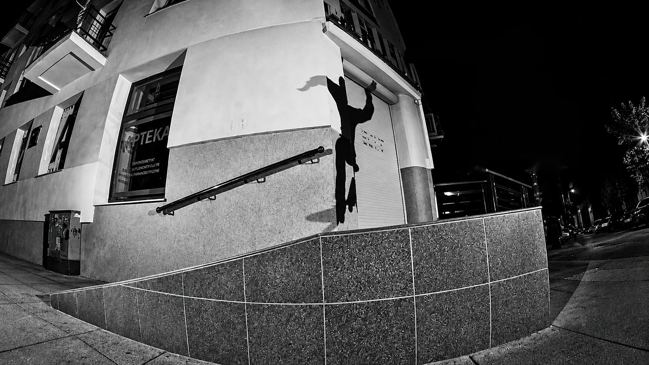 Nocna sesja: skater w wysokim skoku obok granitowego podjazdu przy narożnej kamienicy na Świętojańskiej, czarno-białe zdjęcie